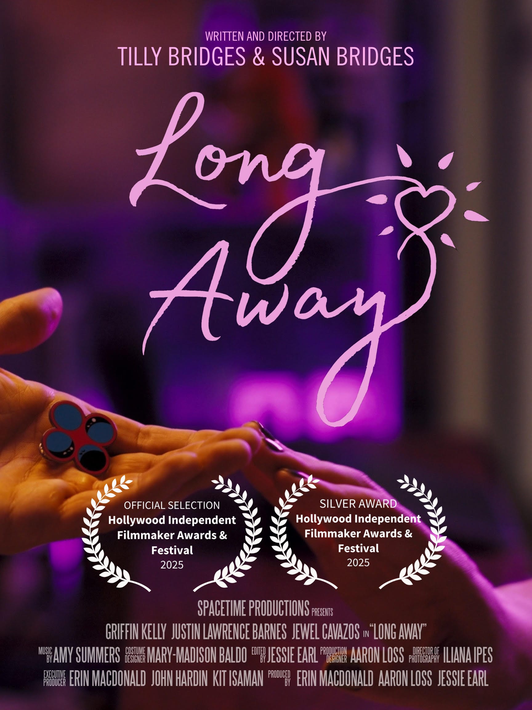 one hand reaching out, palm upward, holding an enamel pin displaying four circles, and another hand reaching out, palm downward, the two hands touch at the fingertips and are bathed in pink light. text reads: LONG AWAY WRITTEN AND DIRECTED BY TILLY BRIDGES & SUSAN BRIDGES SPACETIME PRODUCTIONS PRESENTS GRIFFIN KELLY JUSTIN LAWRENCE BARNES JEWEL CAVAZOS in “LONG AWAY” MUSIC BY AMY SUMMERS COSTUME DESIGN MARY-MADISON BALDO EDITED BY JESSIE EARL PRODUCTION DESIGNER AARON LOSS DIRECTOR OF PHOTOGRAPHY ILIANA IPES EXECUTIVE PRODUCER ERIN MACDONALD JOHN HARDIN KIT ISAMAN PRODUCED BY ERIN MACDONALD AARON LOSS JESSIE EARL&nbsp; official selection and silver award, hollywood independent filmmaker awards & festival 2025